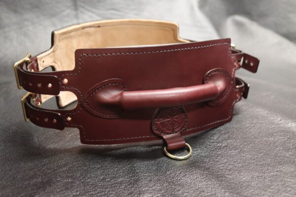 Burgundy English Bridle leather Owned Riding Belt with raised control handle, Royal Star sigil, solid brass hardware, dual side straps, and light leather lining visible inside.