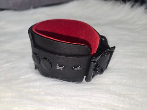 Cuff Closeup 2 Close-up of a black leather Owned Wrist Cuff showing stitching, lining, buckle, and attachment hardware.