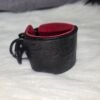 Cuff Closeup 3 Close-up of a black English Bridle leather Owned Riding Wrist Cuff with red deersplit lining, black hardware, and “Good Girl” embossing, showing the cuff’s naturally curved shape.