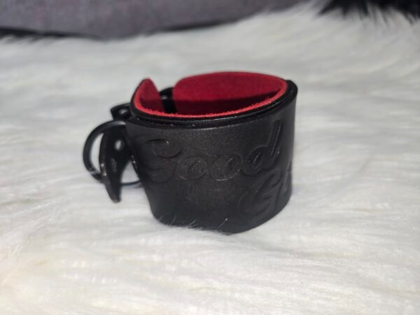 Cuff Closeup 3 Close-up of a black English Bridle leather Owned Riding Wrist Cuff with red deersplit lining, black hardware, and “Good Girl” embossing, showing the cuff’s naturally curved shape.