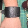 Cuff - Good Girl - Worn 1 Black English Bridle leather Owned Riding Wrist Cuff worn on the wrist, embossed “Good Girl,” showing the cuff’s wide body-shaped fit and curved construction.