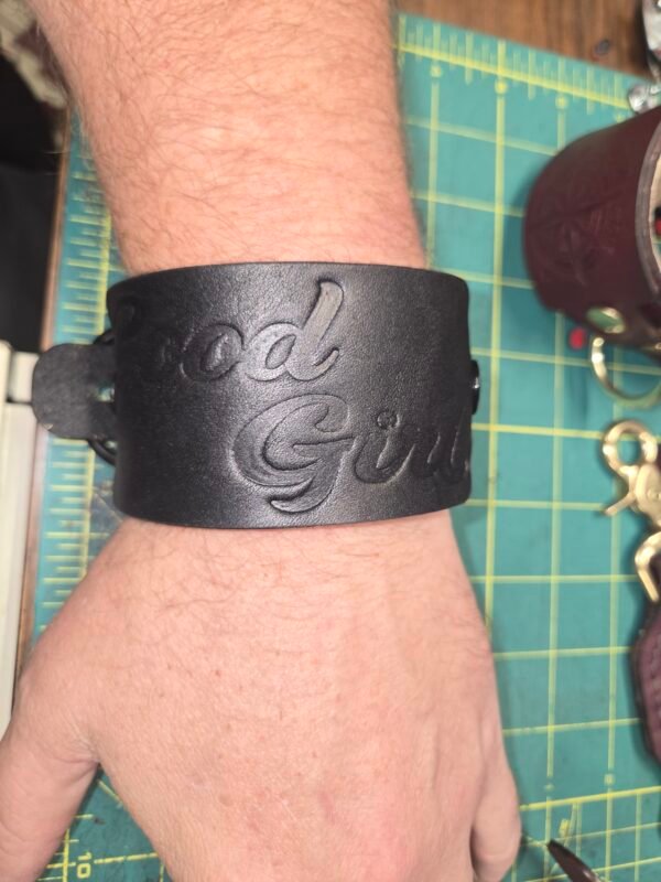 Cuff - Good Girl - Worn 1 Black English Bridle leather Owned Riding Wrist Cuff worn on the wrist, embossed “Good Girl,” showing the cuff’s wide body-shaped fit and curved construction.