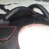 Harness V2.3 Closeup 2 Close-up of the Owned Riding BDSM Harness showing its three-layer leather construction: black 5 oz English Bridle outer, natural 7 oz veg-tan structural core, red 1–2 oz deersplit lining, and raised leather handles for easy grip.