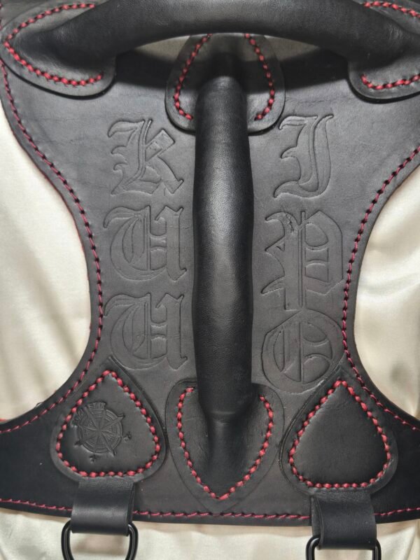 Owned Riding Harness – Black Backpiece Close-Up Black leather Owned Riding BDSM Harness with red stitching, horizontal and vertical handles, two D-ring attachment points, and custom embossing.