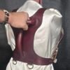 Harness v2.3 - on Mannequin Burgundy - Hand on 1 Burgundy English Bridle leather Owned Riding BDSM Harness with solid brass D-rings, shown from the rear while the horizontal control handle is being gripped.