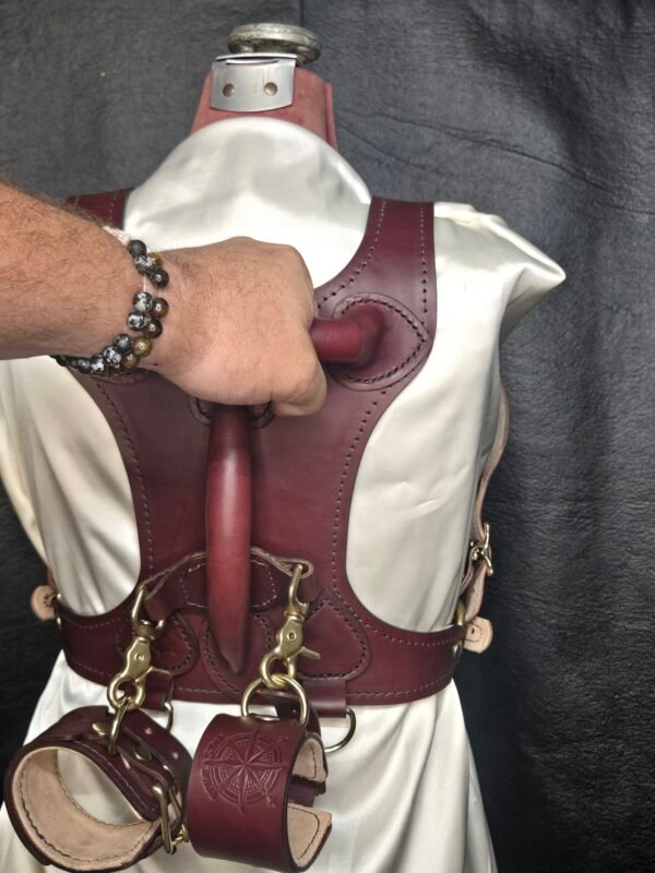 Harness v2.3 - on Mannequin Burgundy - Hand on 2 Burgundy English Bridle leather Owned Riding BDSM Harness with solid brass hardware, shown from the rear with a tether routed through the vertical handle opening and cuffs attached below.
