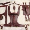 Owned Riding Rig laid out on a white fur background, including the Burgundy English Bridle Owned Riding Harness, Owned Riding Belt, Owned Riding Cuffs, Drop Tip Sigil Collar, and matching tether, all finished with solid brass hardware.