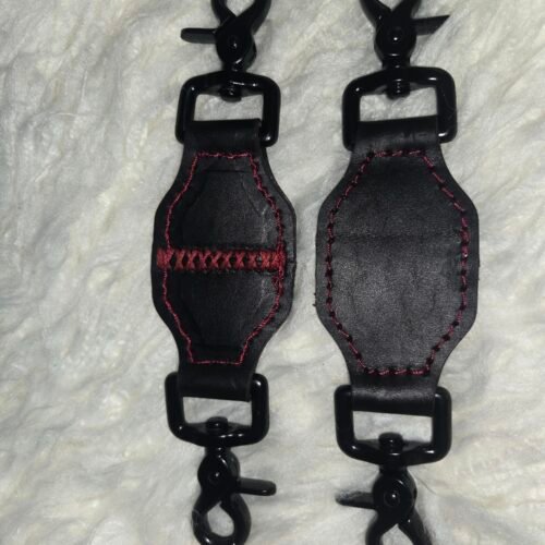 Pair of black English Bridle leather tethers with red stitching and black swivel snap hardware, shown laid flat on a white fur background.